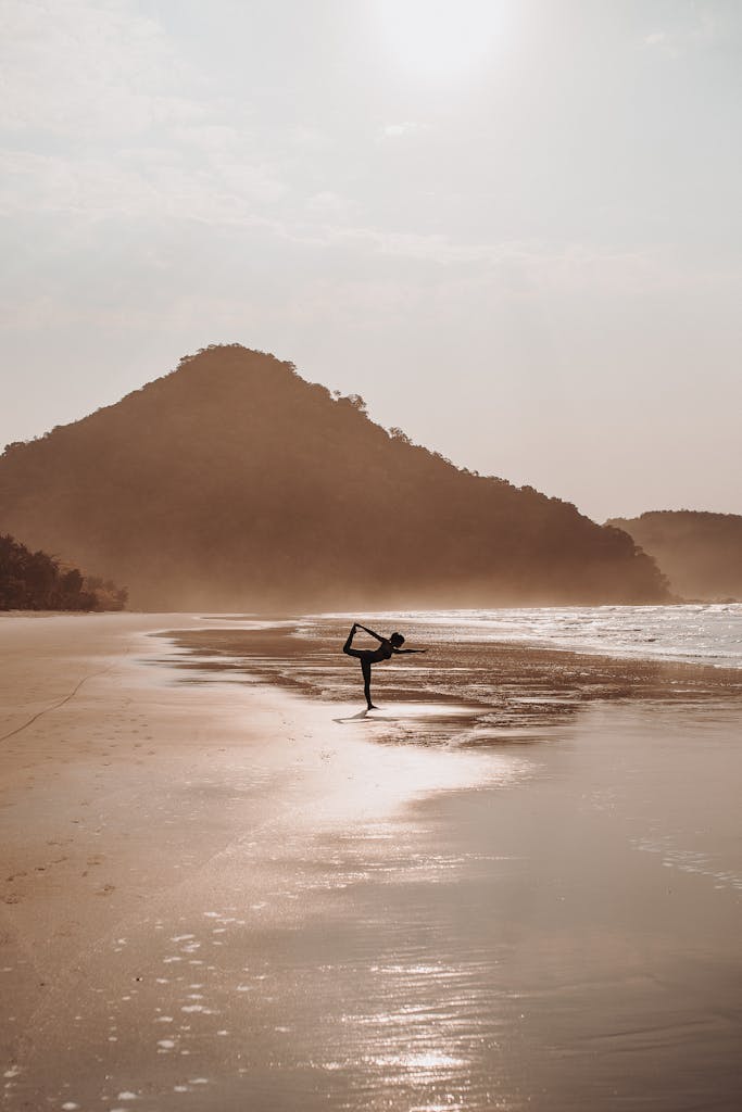 Silhouette of a woman practicing yoga on a tranquil beach during sunrise.